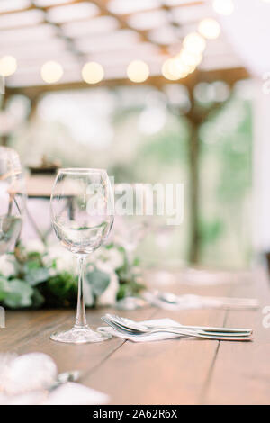 Rustikale Tische mit Blumenschmuck, Laternen. Weingläser auf dem Tisch. Hochzeit oder Tisch im Restaurant im Freien Stockfoto