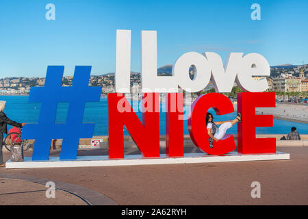 Eine dunkelhaarige Frau touristische stützt auf den Buchstaben "c" in der berühmten Zeichen entlang der Küste der französischen Riviera in Nizza, Frankreich. Stockfoto