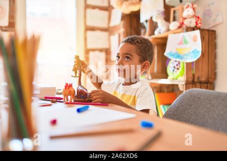 Schöne afrikanische amerikanische Kleinkind spielen mit Dinosaurier Spielzeug auf dem Schreibtisch im Kindergarten Stockfoto