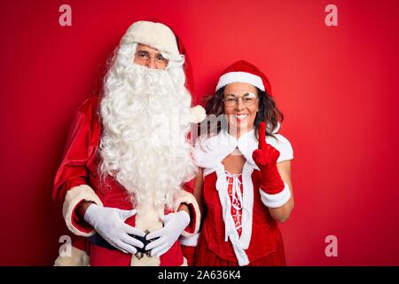 Mittleres Alter Paar Tragen santa Kostüm und Gläser über isolierten roten Hintergrund angezeigt und zeigt mit dem Finger Nummer eins beim Lächeln werden. Stockfoto