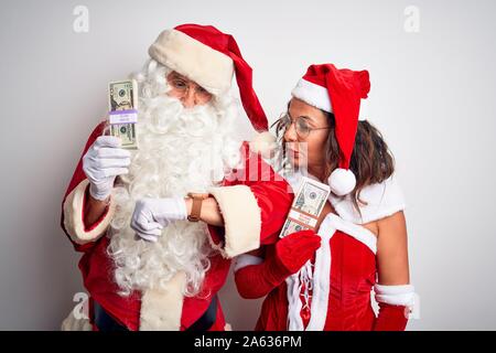 Senior Paar Tragen santa claus Kostüm holding Dollar über isoliert weißer Hintergrund Kontrolle der Zeit auf Armbanduhr, entspannt und zuversichtlich Stockfoto