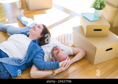 Junges Paar in Liebe auf dem Boden des neuen Hauses rund um Kartonagen, Lächeln sehr glücklich für den Umstieg auf eine neue Wohnung Stockfoto