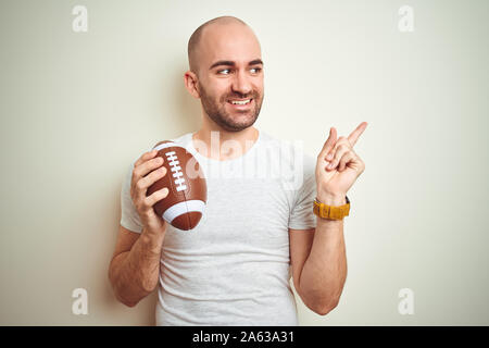 Junger Mann, Rugby, American Football Ball über isolierte Hintergrund sehr zufrieden zeigt mit Finger- und an der Seite Stockfoto