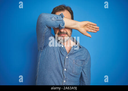 Stattliche mittleren Alters älterer Mann mit dem grauen Haar über isolierte blauen Hintergrund, die Augen mit Arm, ernst und traurig. Sightless, Verstecken und Rej Stockfoto