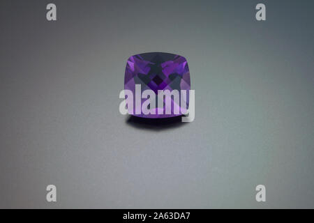 Eine pin-gepolsterten Square Cut Amethyst ist auf einem grauen reflektierenden Hintergrund dargestellt. Stockfoto