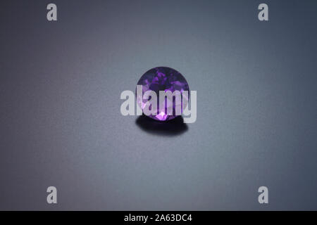 Eine runde Amethyst ist auf einem grauen reflektierenden Hintergrund dargestellt. Stockfoto