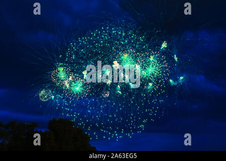 Preiswertes Feuerwerk über der Stadt Rot, Grün und Gelb auf den blauen Himmel. Hell und glänzend. Für jeden Zweck. Feier Konzept. Stockfoto