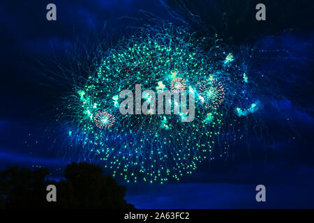 Preiswertes Feuerwerk über der Stadt Rot, Grün und Gelb auf den blauen Himmel. Hell und glänzend. Für jeden Zweck. Feier Konzept. Stockfoto