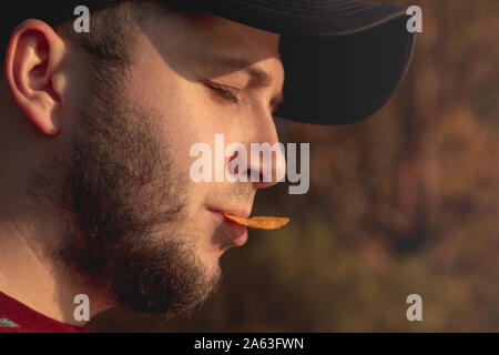Bearder Mann im Wald essen Chips. Im Park Bild im Freien mit unscharfem Hintergrund. Stockfoto
