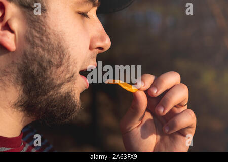 Bearder Mann im Wald essen Chips. Im Park Bild im Freien mit unscharfem Hintergrund. Stockfoto