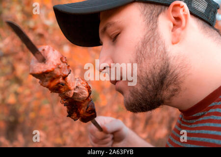 Der Mensch ist Shish Kebab zu essen. Der bärtige Mann ißt ein Shish Kebab riss ihn aus den Spieß mit seinen Mund. Stockfoto