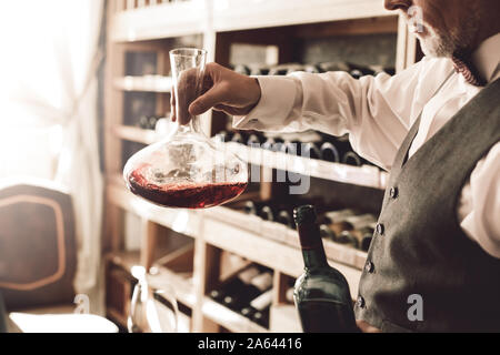 Sommelier Konzept. Älterer Mann Dekanter rühren Wein in der Karaffe nachdenkliche Seite close-up Stockfoto