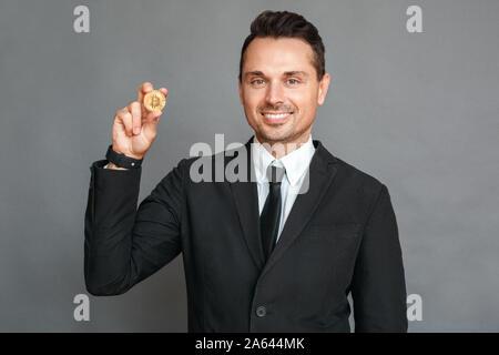 Geschäftsmann Studio stehen isoliert auf grau angezeigt cryptocurrency Münze lächelt glücklich Stockfoto