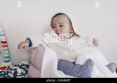 Verärgert baby boy trägt einen Pullover sitzen im Stuhl und wartet Mutter zu Hause Stockfoto