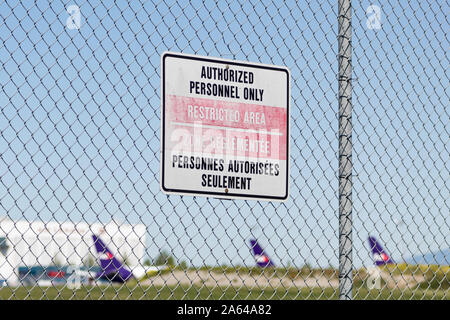 Nur autorisiertes Personal/eingeschränkter Bereich - französische und englische Zeichen an einem Zaun außerhalb von Vancouver Intl. Flughafen mit Flugzeug im Hintergrund. Stockfoto