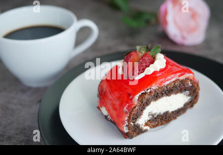 Schokoladenkuchen mit Erdbeermarmelade Sauce garniert mit Schlagsahne und frischen Erdbeeren gehackt auf weiße Platte mit einer Tasse schwarzen Kaffee serviert, blur Stockfoto