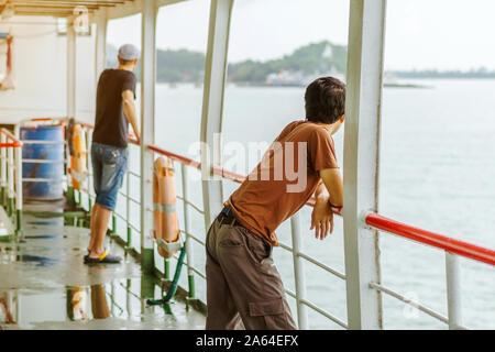 Asiatischer Mann steht auf Kunst Elemente der Fähre zum Entspannen und auf das Meer und die Insel. Stockfoto