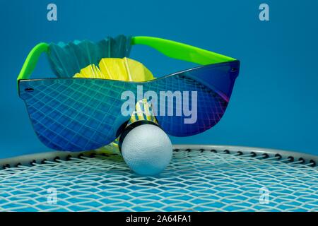 Bunt gefiederten Badminton Federball mit Sonnenbrille ruht auf einem Schläger auf einem blauen Hintergrund in der Nähe zu Still Life Stockfoto