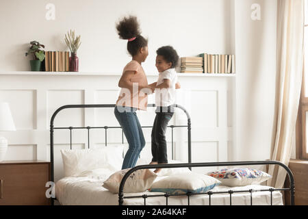 Aktive Schwarze Bruder und Schwester springen Sie auf Bett zusammen Stockfoto