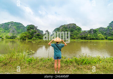 Frau mit vietnamesischen Hut auf einzigartige Aussicht von Tam Coc Trang Ein Ninh Binh Reiseziel in Vietnam suchen. Karst rock pinnacles zwischen den Reisfeldern. Stockfoto