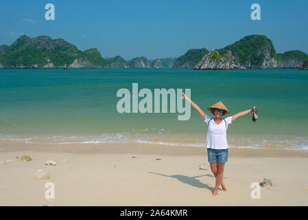 Frau mit vietnamesischen Hut auf Monkey Island Beach Cat Ba Halong Bay, Vietnam. Touristische Reisen auf Kreuzfahrt unter Ha Long Bay rock Pinnacles im Meer. Stockfoto