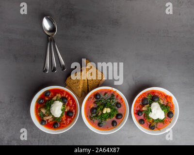 Ukrainische traditionellen Borschtsch. Russische vegetarische rote Suppe in weißen Schüsseln auf grauen Hintergrund. mit schwarzen Oliven, Knoblauch, Schmalz, Brotscheiben Ansicht von Oben. C Stockfoto