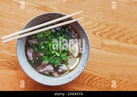 Köstliche warme vietnamesische Nudelsuppe Pho Bo in einer Schüssel auf hölzernen Tisch Stockfoto