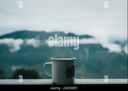 Nahaufnahme zum Reisenden Metallbecher mit heißem Tee auf dem Balkon der Hütte in den Bergen. Dampf verdunstet. Reisekonzept. Getränk während der Fahrt. Stockfoto