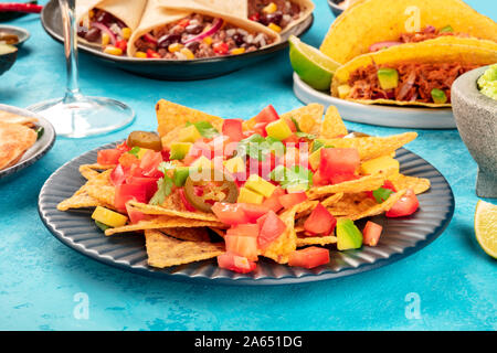 Nachos mit Avocado und Tomaten, mit jalapeno Pfeffer und Koriander Blätter, auf einem Tisch mit anderen mexikanischen Essen Stockfoto