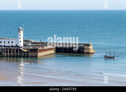 Der Weiße Leuchtturm am Ende des Hafenpiers zusammen mit einem Piratenschiff, das in Scarborough North Yorkshire England, Großbritannien, in See fährt Stockfoto