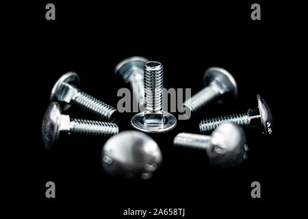Gruppe von metallisch glänzenden Schrauben auf schwarzem Hintergrund kreisförmig angeordnet Stockfoto