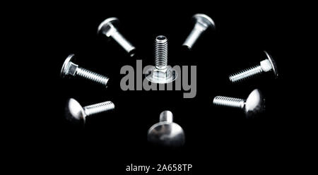 Eine Menge metallisch glänzenden Schrauben auf schwarzem Hintergrund in einer kreisförmigen und konzentrische Form angeordnet sind Stockfoto