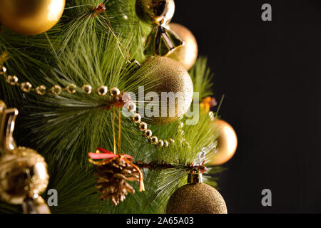 Weihnachtsbaum Detail mit goldenen Ornamenten mit schwarzem Hintergrund beleuchtete eingerichtet. Horizontale Komposition. Ansicht von vorn Stockfoto