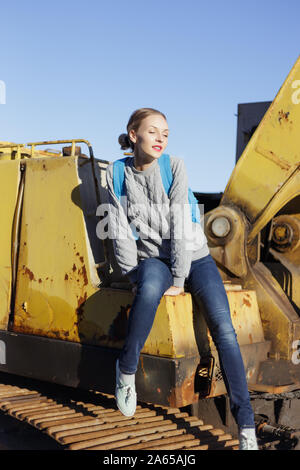 Junge Frau sitzt auf einem gelben Bagger. Stockfoto