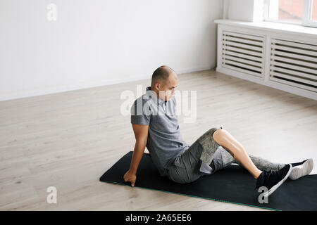 Junger Mann mit Prothese sitzt auf trainingsmatte und Ausruhen nach Sport Training Stockfoto