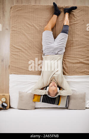 Hohe Betrachtungswinkel von behinderten Menschen in Kopfhörer Musik hören und Entspannen auf dem Bett im heimischen Zimmer Stockfoto