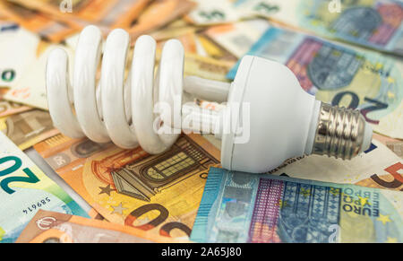 Metapher über die übermäßigen Kosten von Licht, Energie und Strom, mit einem weißen Halogenlampe auf einem Bett von Zwanzig und fünfzig Euro Rechnungen Stockfoto