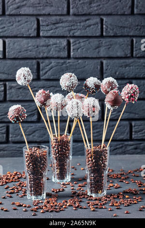 Hausgemachte Schokolade Kuchen pops bestreut mit zerquetschten Bonbons und Kokosnuss Gitterboxen sollten in drei Gläser mit Kaffee Körner auf einer konkreten Tabelle. Ein schwarzes Bri Stockfoto