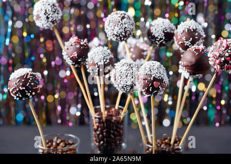 Hausgemachte Schokolade Kuchen pops bestreut mit zerquetschten Bonbons und Kokosnuss Gitterboxen sollten in drei Gläser mit Kaffee Körner auf einer konkreten Tabelle mit Colorfu Stockfoto