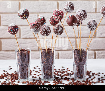 Hausgemachte Schokolade Kuchen pops bestreut mit zerquetschten Bonbons und Kokosnuss Gitterboxen sollten in drei Gläser mit Kaffee Körner auf einer konkreten Tabelle. Licht brick Stockfoto