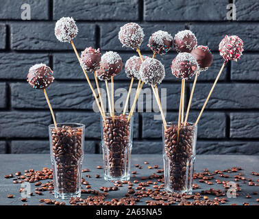 Festliche Schokoladenkuchen pops bestreut mit zerquetschten Bonbons und Kokosnuss Gitterboxen sollten in drei Gläser mit Kaffee Körner auf einer konkreten Tabelle. Ein schwarzes bric Stockfoto