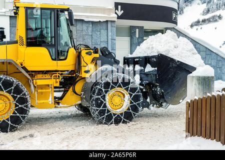 Big loader Maschine mit Stahl Ketten aus Metall entfernen von großen Schnee Haufen vom city street bei alpine Bergwelt im Winter. Starker Schneefall Nachwirkungen Stockfoto