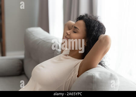 Ruhige schwarze junge Frau auf dem Sofa die Hände über dem Kopf entspannen Stockfoto