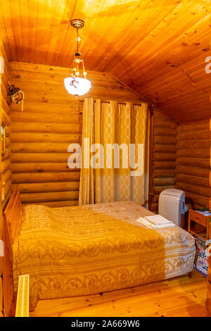 Hotel Einfaches Einzelzimmer mit orangefarbenen Vorhang Bettwäsche und hölzerne Wände Stockfoto