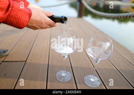 Männliche Hände im roten Hemd gießen Wein auf Holztisch. Stockfoto
