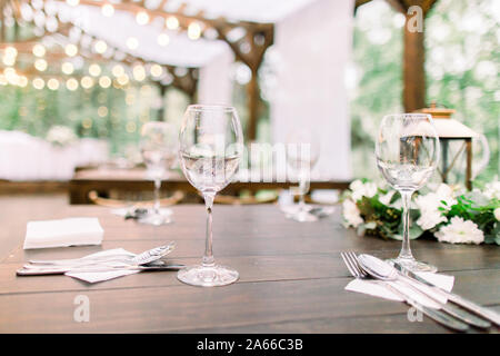 Rustikale Tische mit Blumenschmuck, Laternen. Weingläser auf dem Tisch. Hochzeit oder Tisch im Restaurant im Freien Stockfoto