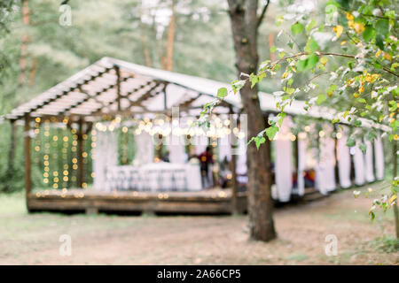 Verschwommenes Foto von hölzernen Hütte Restaurant mit Holztischen und -stühlen., mit Glühbirnen Vintage Design des Restaurants in den Wald in eingerichtet Stockfoto