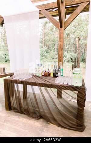 Catering. Getränke auf der Hochzeitsfeier. Viele Gläser, Flaschen mit Alkohol auf dem Tisch, auf dem Hintergrund der im Außenbereich Restaurant im Wald Stockfoto