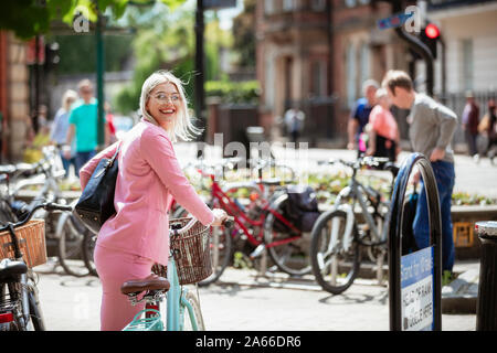 Eine Geschäftsfrau zurück schauen in die Kamera, während sie auf einem Fahrrad, bereit, es zu fahren. Stockfoto