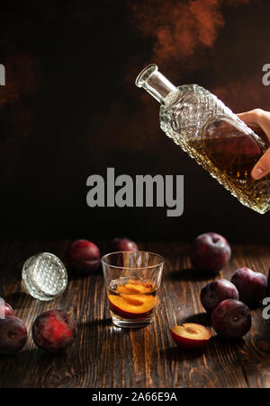 Schnaps oder Rakija traditionellen Balkan Obst Schnaps. Plum Schnaps sljivovica in ein Glas und Karaffe auf dem Tisch. Schnaps aus einer Flasche in ein Glas gegossen Stockfoto